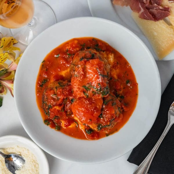 Italian meatballs in rich tomato sauce with parmesan, wine, and prosciutto on a white table.