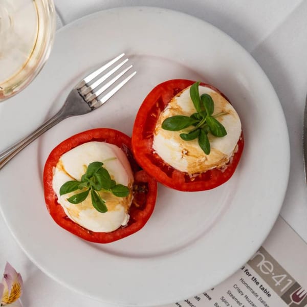 Two halves of red tomatoes filled with mozzarella, drizzled with balsamic glaze and garnished with basil.