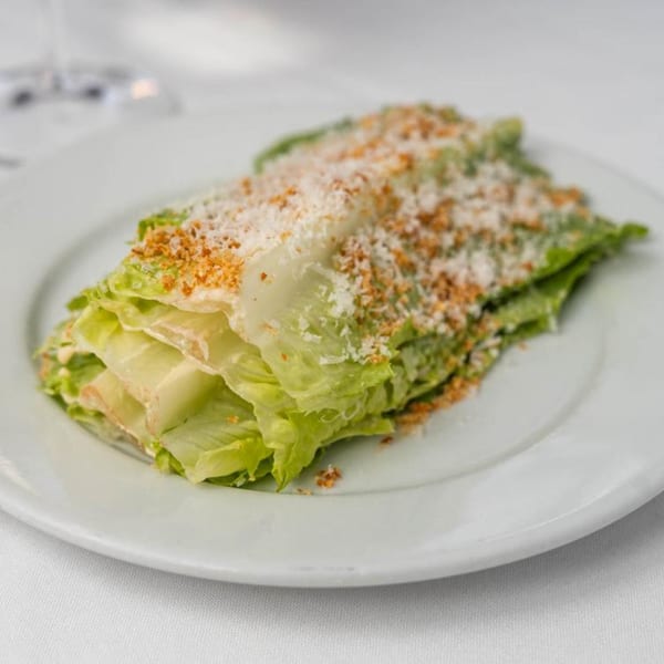 A fresh Caesar salad with crisp romaine lettuce, parmesan cheese, and croutons on a white plate.
