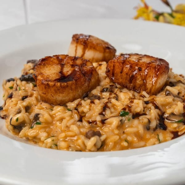 Seared scallops with a balsamic glaze on a bed of creamy mushroom risotto, served on a white plate.