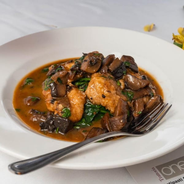 Italian chicken and mushrooms in a rich brown sauce with spinach, served in a white bowl.