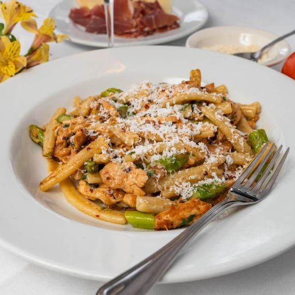 A plate of Italian pasta with chicken, green vegetables, and grated cheese, with a fork beside it.