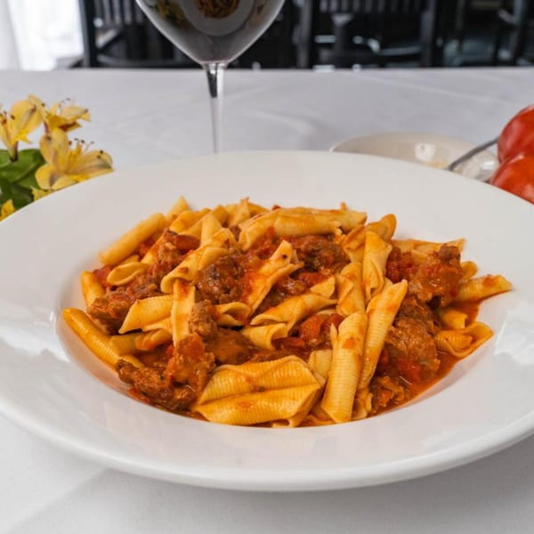 A white plate of Italian pasta with meat sauce, a glass of red wine, and yellow flowers.